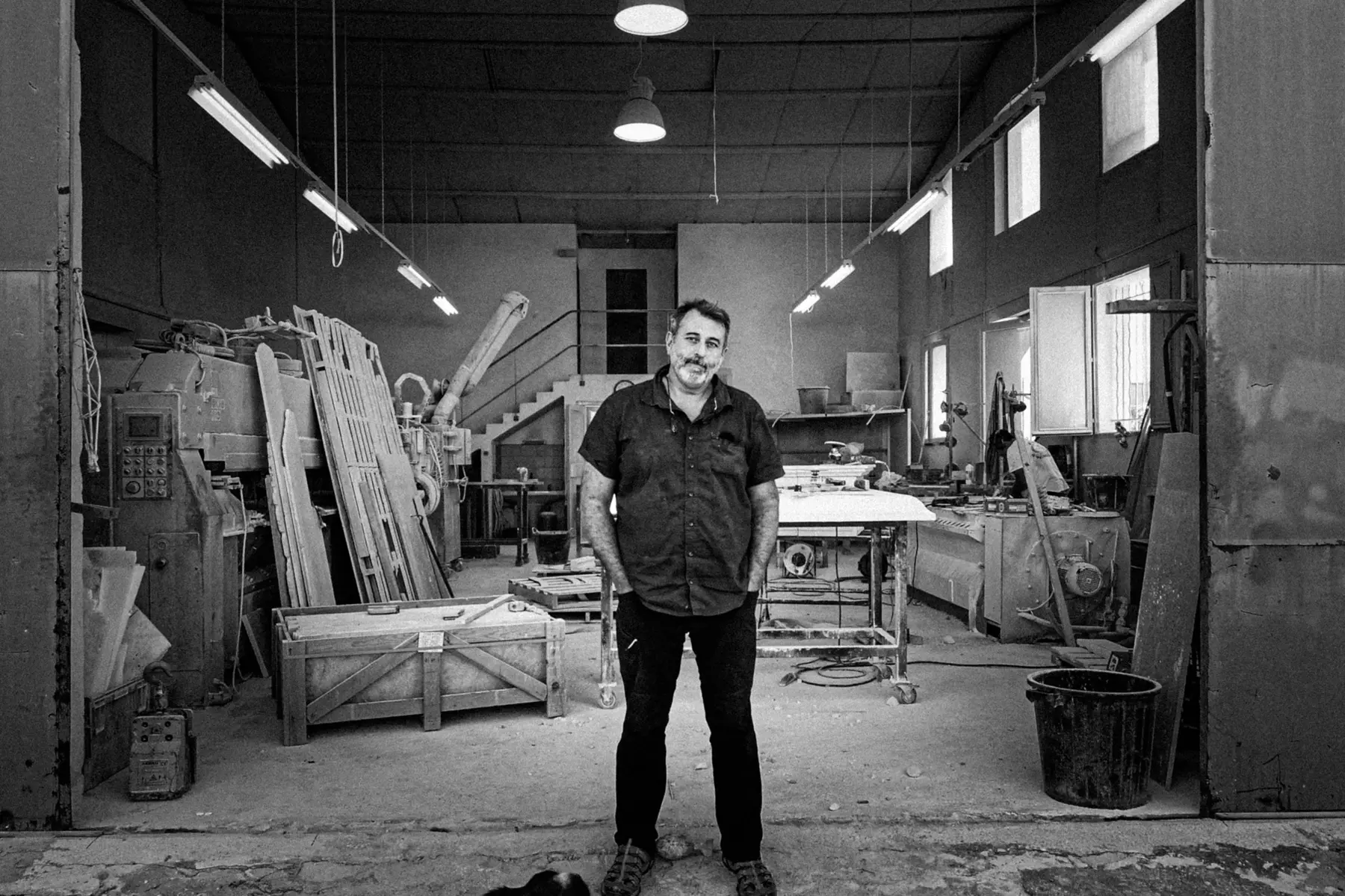 Artisan debout au centre de son atelier, entouré de ses machines et de ses outils
