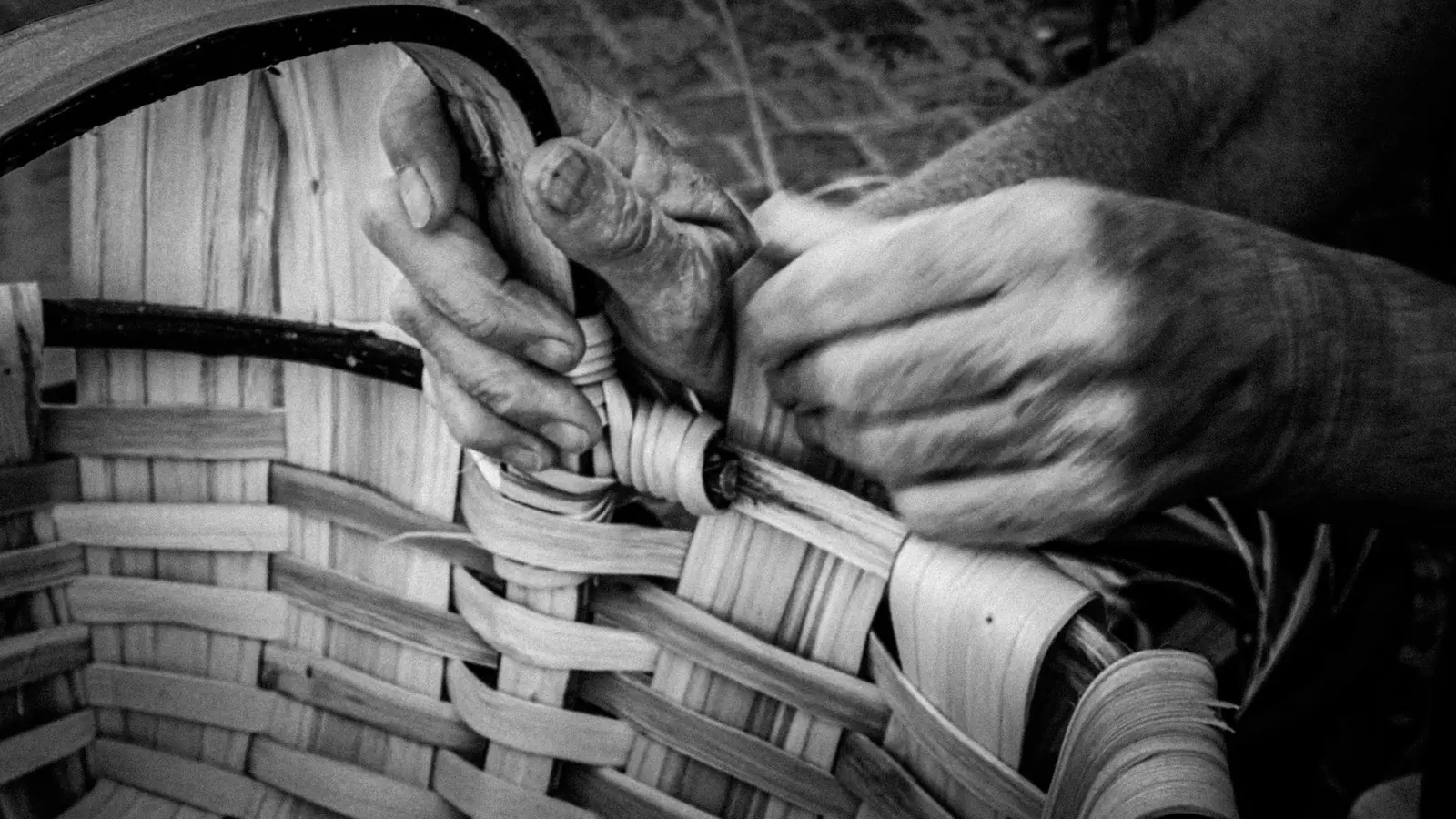 Mains d’une vannière assemblant les fibres d’un panier